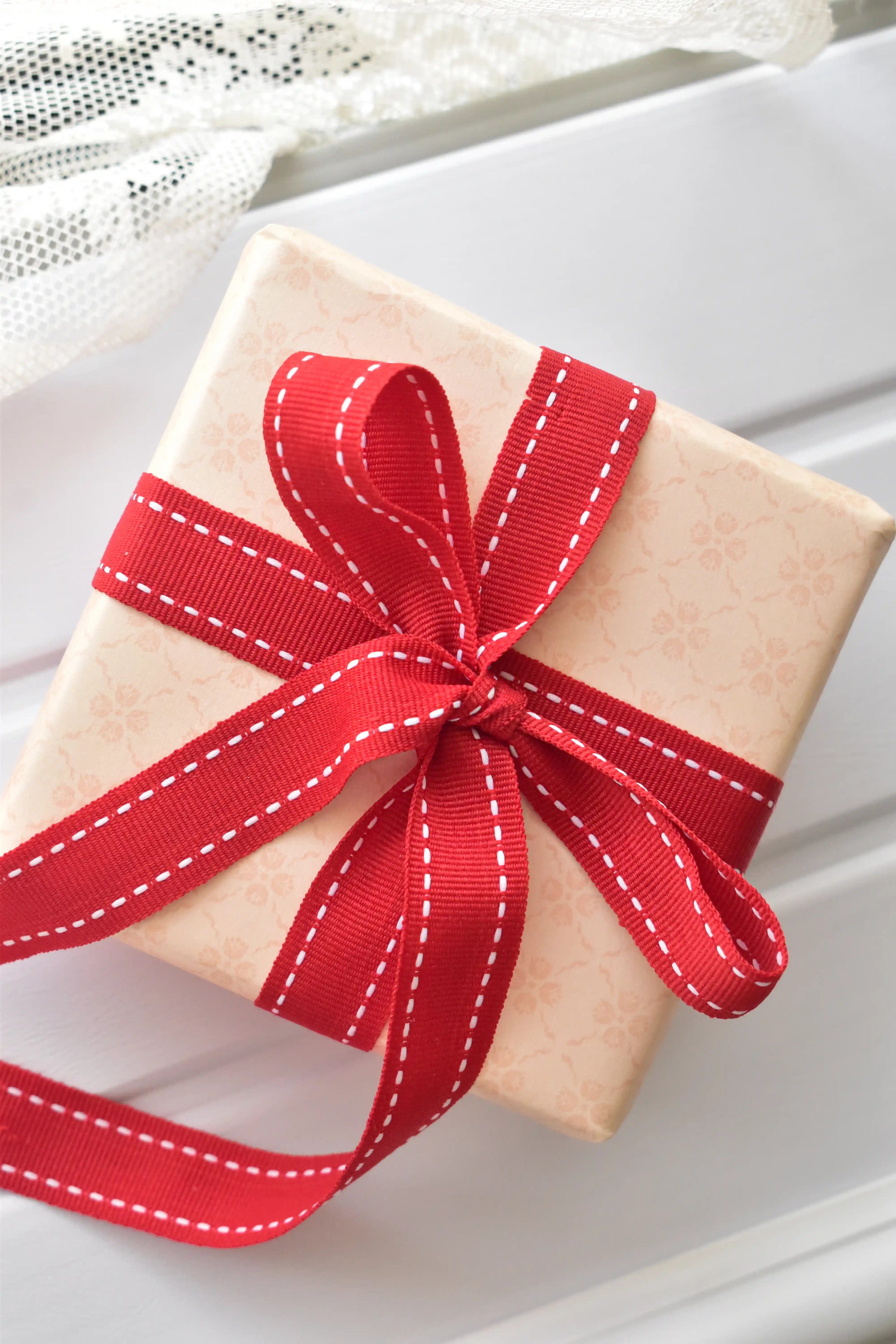 A top-down view of a light-patterned gift box decorated with a beautiful bow made from the Berry Stitch red ribbon. The image shows how the ribbon can be used for gift wrapping.

