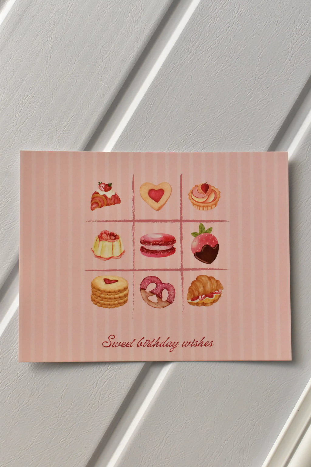 This image showcases the front of the Birthday Bakes Postcard, highlighting the vibrant grid of nine different baked goods and the soft pink striped background.
