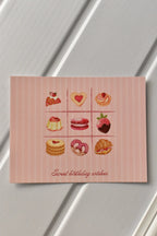 This image showcases the front of the Birthday Bakes Postcard, highlighting the vibrant grid of nine different baked goods and the soft pink striped background.