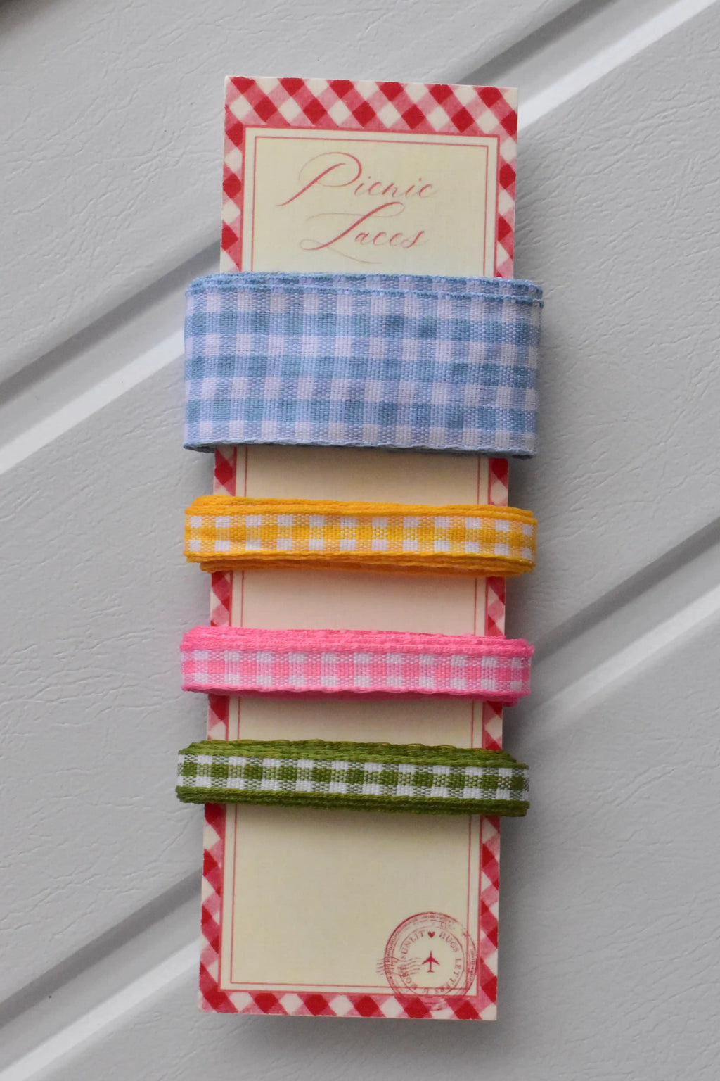 Four narrow gingham ribbons in blue, yellow, pink, and green colours, displayed vertically on a themed ribbon card.