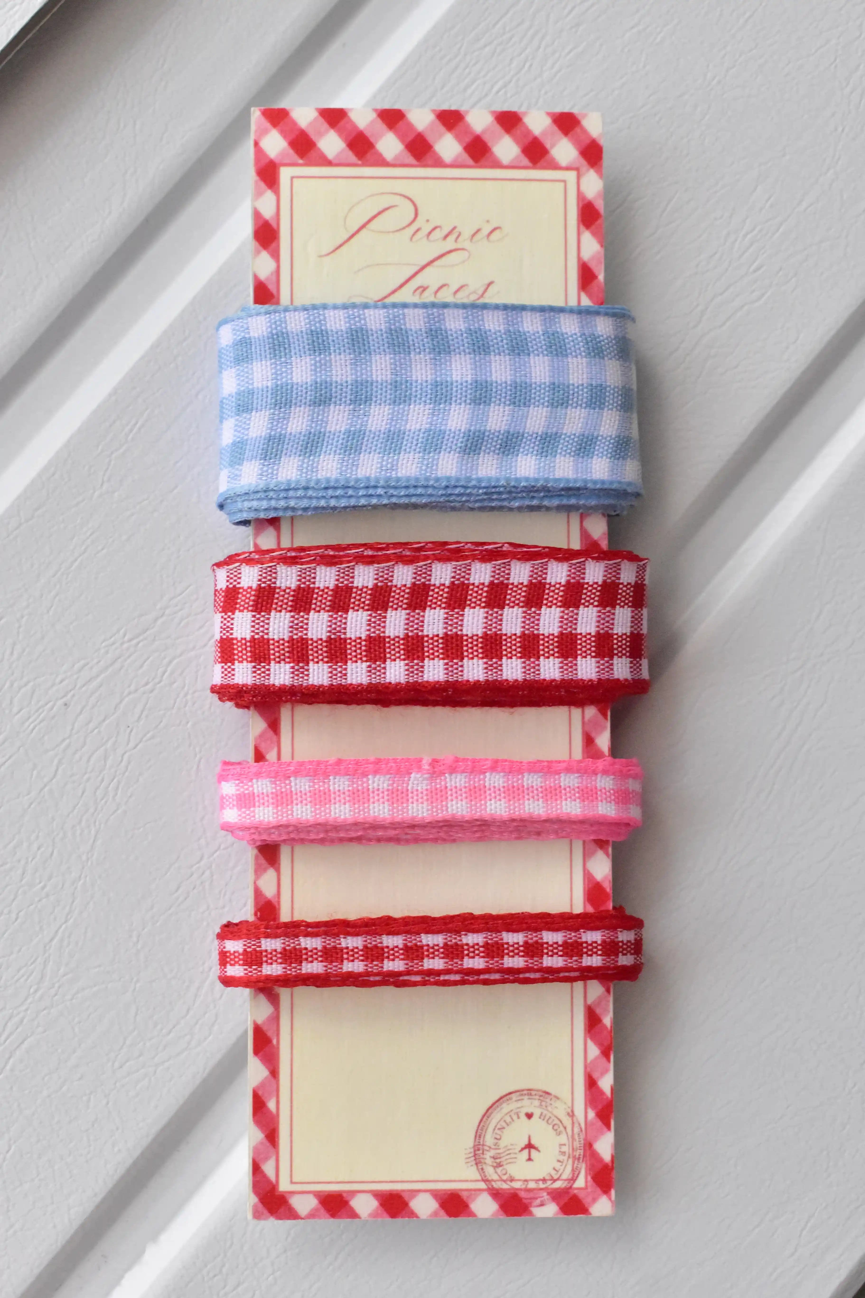 Four gingham ribbons—wide light blue, wide red, narrow pink, and narrow red—displayed vertically on a themed ribbon card.