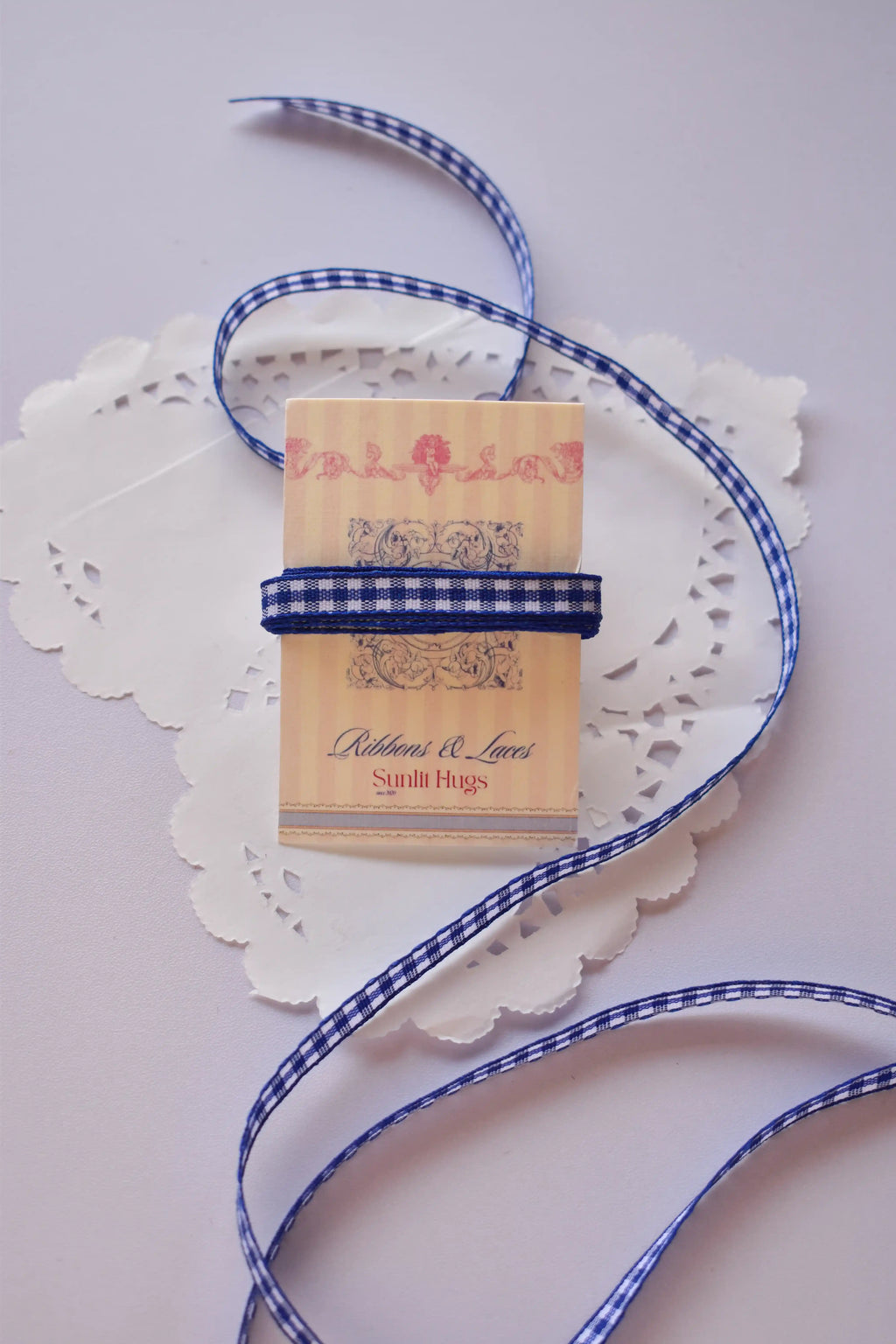 Narrow navy blue and white gingham ribbon wrapped around a "Sunlit Hugs" card, with a long, loose strand flowing down.