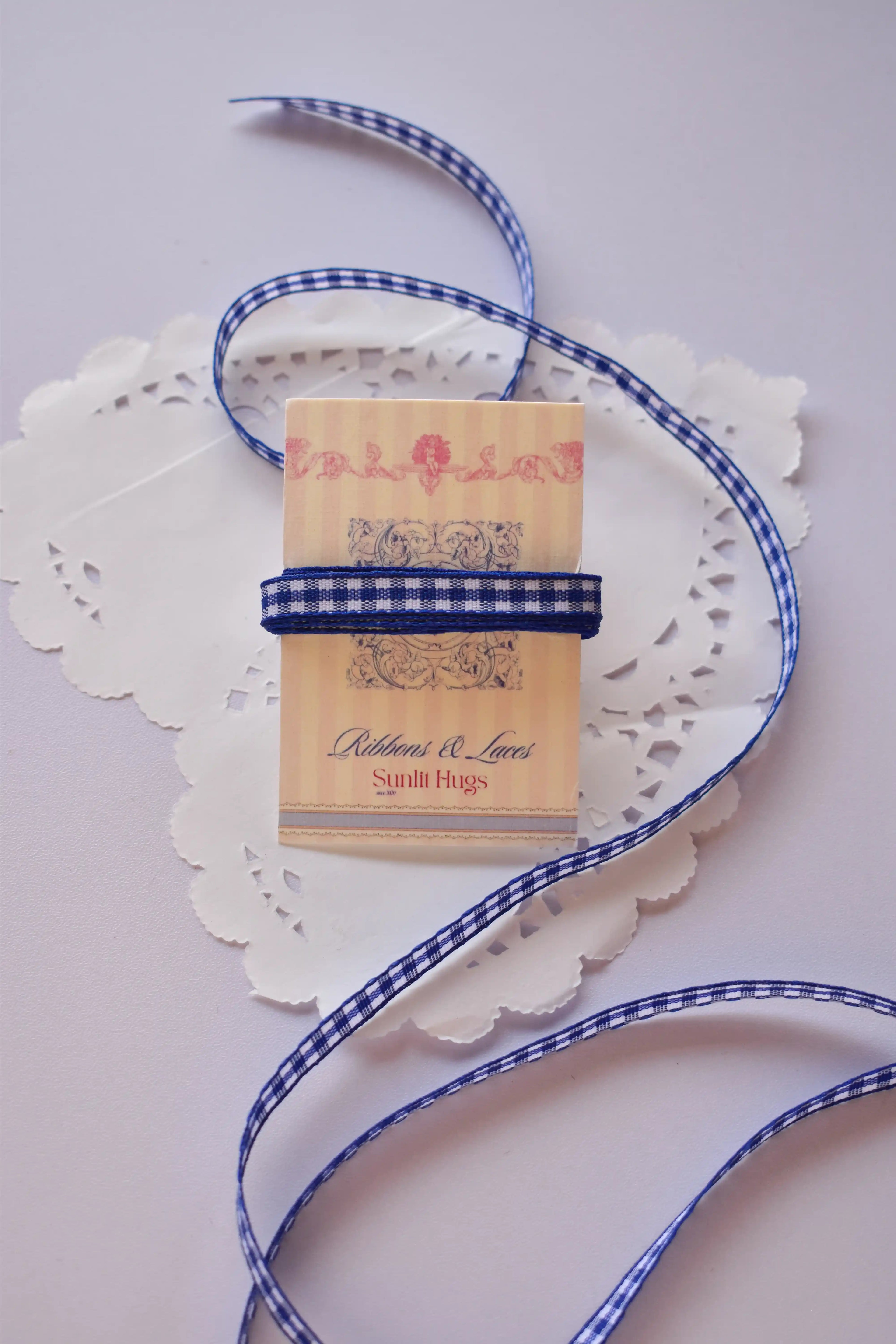 Narrow navy blue and white gingham ribbon wrapped around a "Sunlit Hugs" card, with a long, loose strand flowing down.