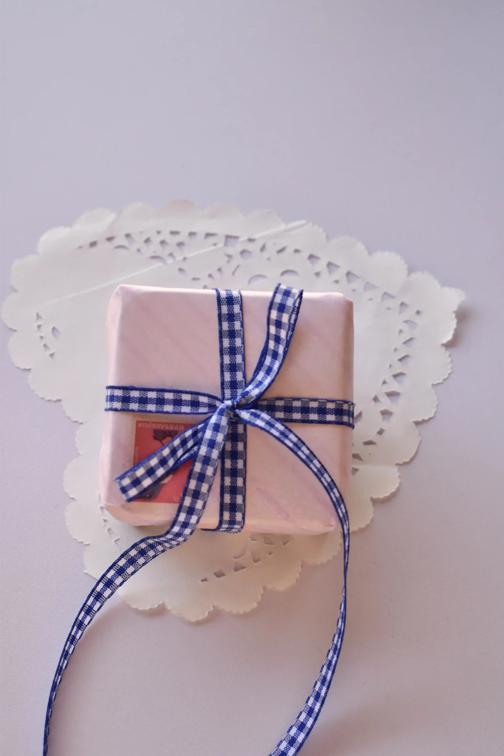 A small, pink striped gift box tied with a narrow navy blue and white gingham ribbon bow.
