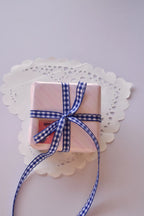 A small, pink striped gift box tied with a narrow navy blue and white gingham ribbon bow.