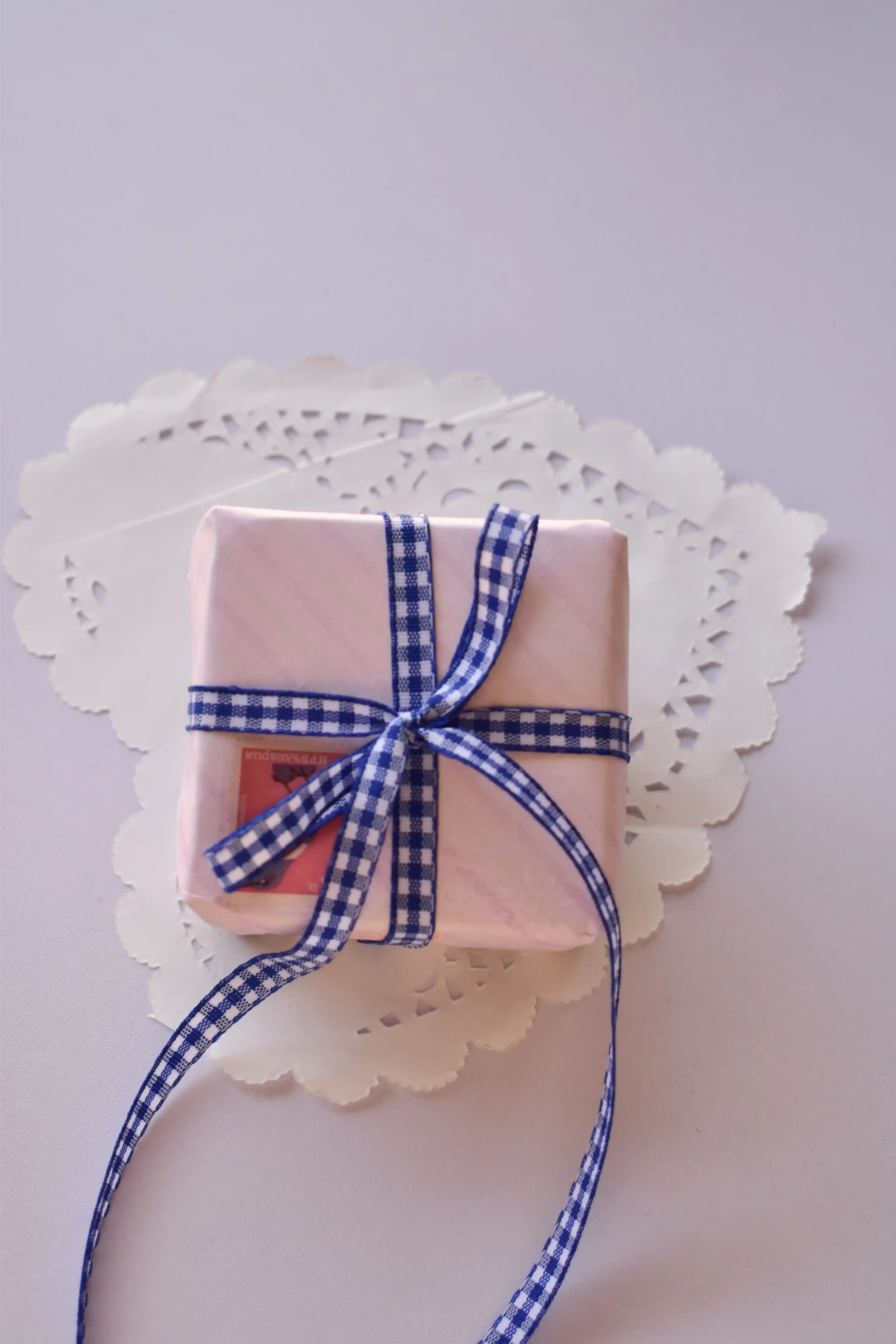 A small, pink striped gift box tied with a narrow navy blue and white gingham ribbon bow.