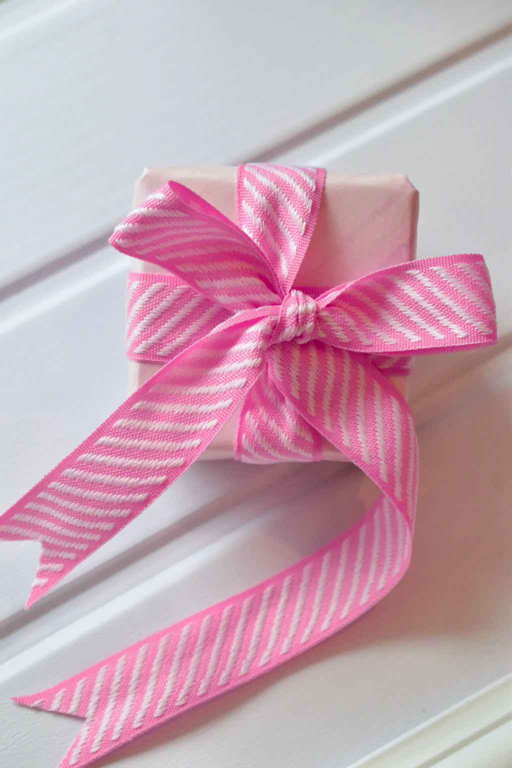 A top-down view of a small, wrapped gift. The Candy Stripes ribbon, with its pink and white diagonal pattern, is tied into a double bow, showcasing its use for gift wrapping.