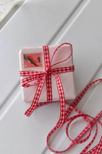  A charming view of a small, light pink wrapped gift box, elegantly tied with the Cherry Picnic narrow red and white checkered ribbon. A vintage-style bird stamp adorns the top, illustrating a creative way to use the ribbon for gift presentation.