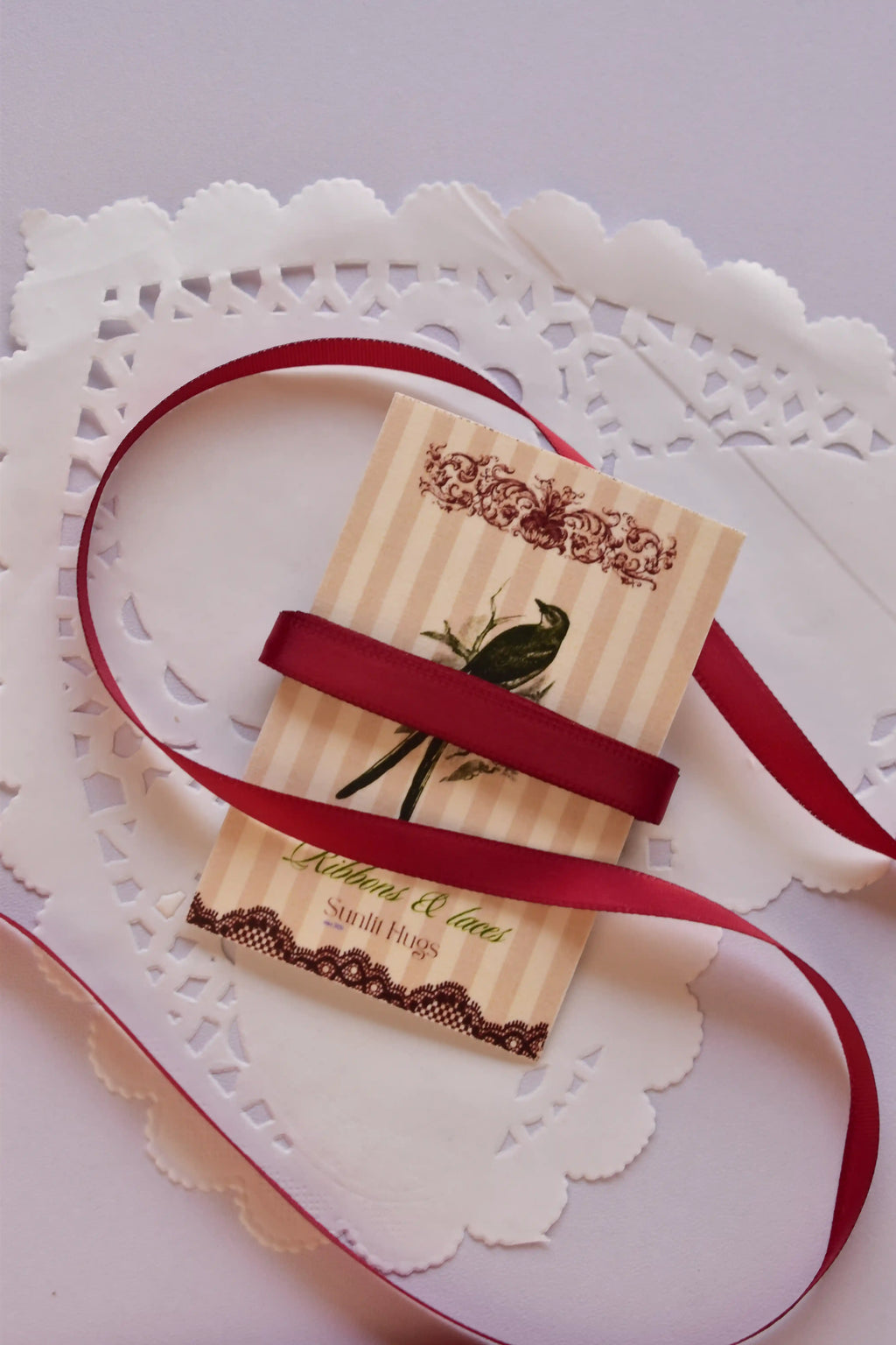 Narrow cherry red satin ribbon (6mm, 2 Metres) wrapped tightly across a "Sunlit Hugs" card, highlighting the sleek, smooth texture.