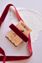 Wide cherry red velvet ribbon (15mm, 2 Metres) draped elegantly around a "Sunlit Hugs" card with a long, loose strand flowing down.