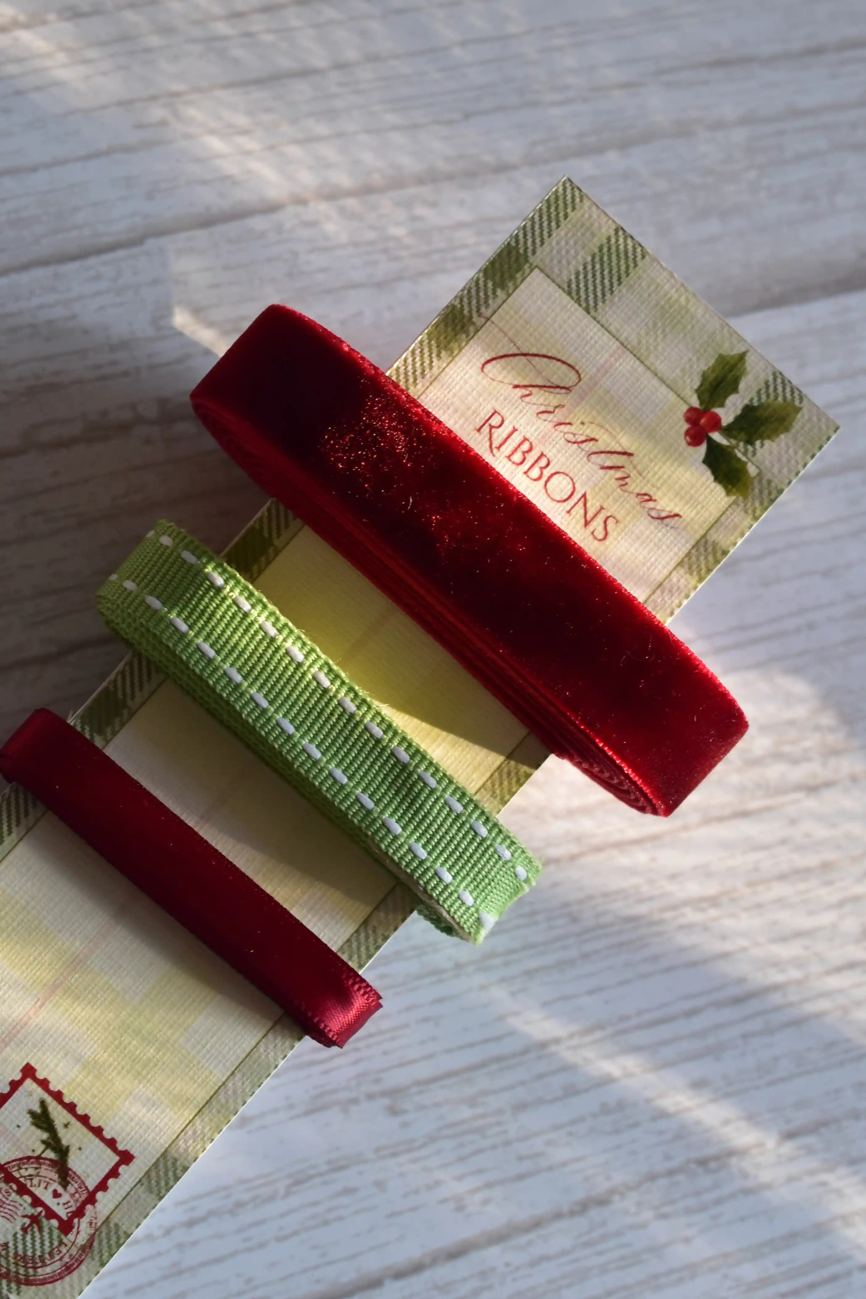An extreme close-up of the three premium Christmas ribbons: deep red velvet, green stitched grosgrain, and thin red satin, displayed on a festive card stock label.