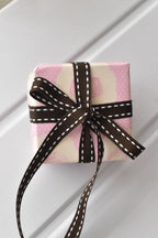 This image shows a beautifully wrapped gift box, featuring the Cocoa Stitch ribbon with its dark brown colour and white dashed stitching, tied into an elegant bow, demonstrating its use for sophisticated gift presentation.