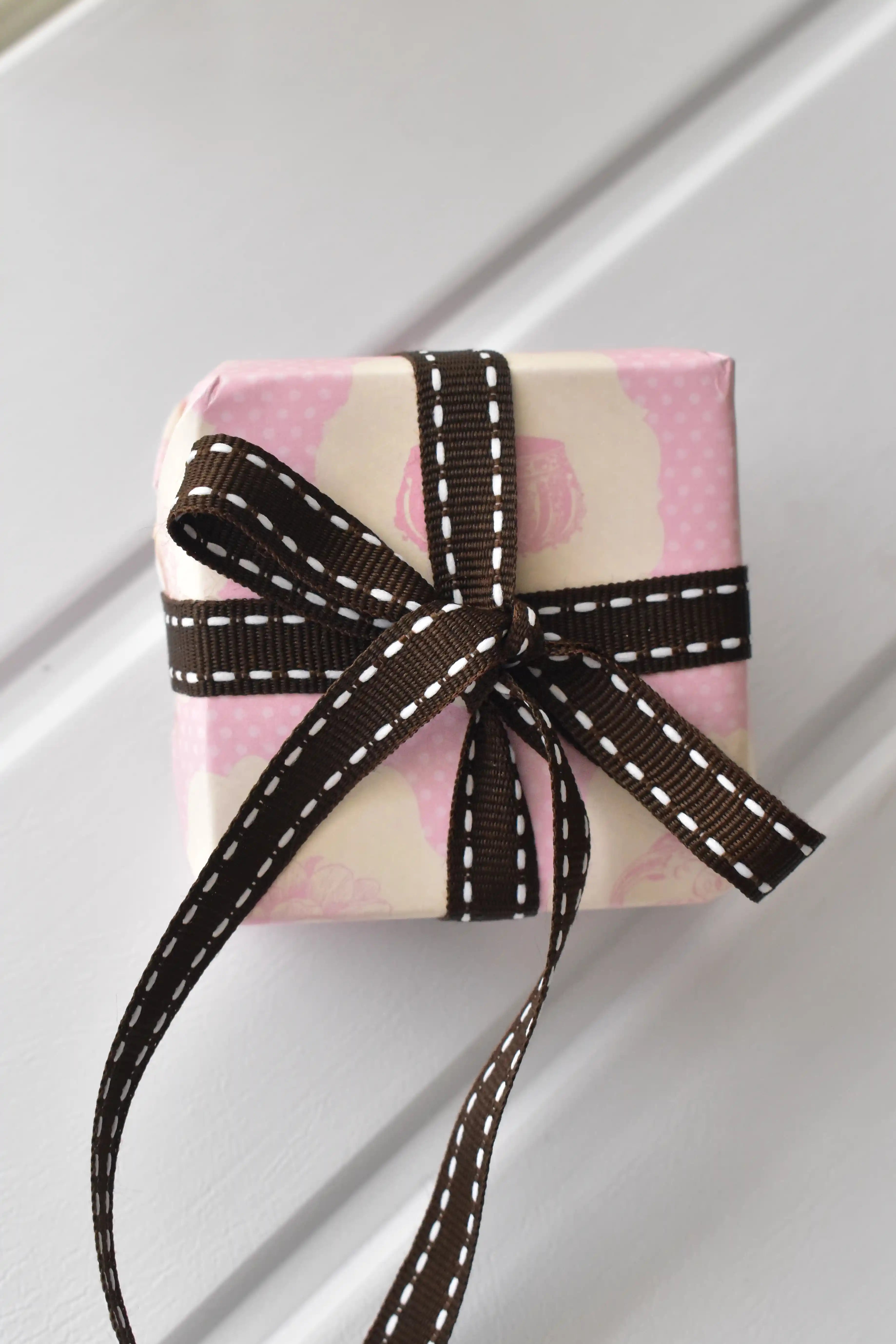 This image shows a beautifully wrapped gift box, featuring the Cocoa Stitch ribbon with its dark brown colour and white dashed stitching, tied into an elegant bow, demonstrating its use for sophisticated gift presentation.