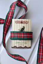 This image displays the Cranberry Trail ribbon with a long, flowing strand, highlighting its red and green plaid pattern and texture. A section is also wrapped around a "Sunlit Hugs" brand tag.