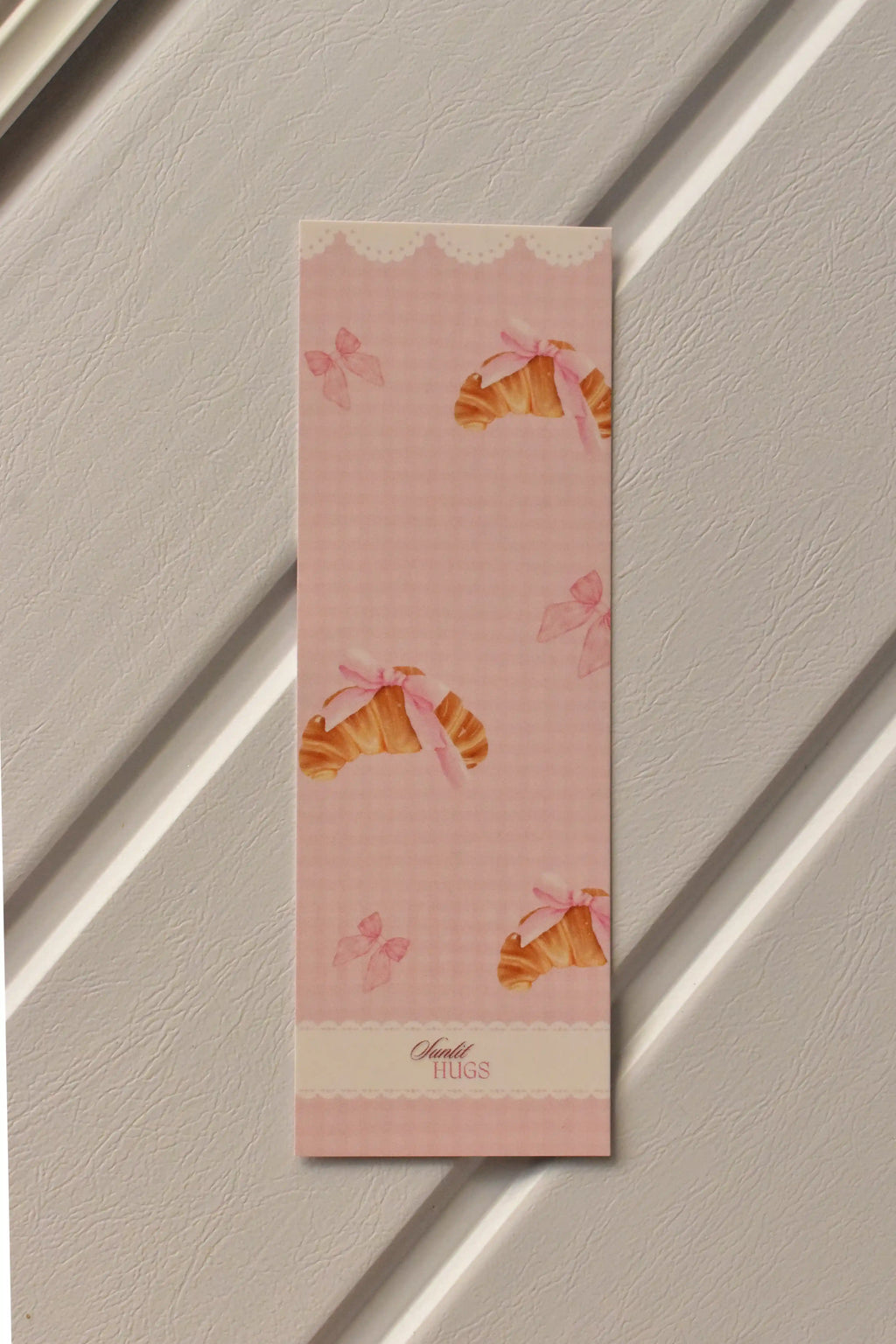 This image shows a detailed, centered view of the Croissant Bookmark front, highlighting the soft pastel pink colour and the charming croissant illustration.
