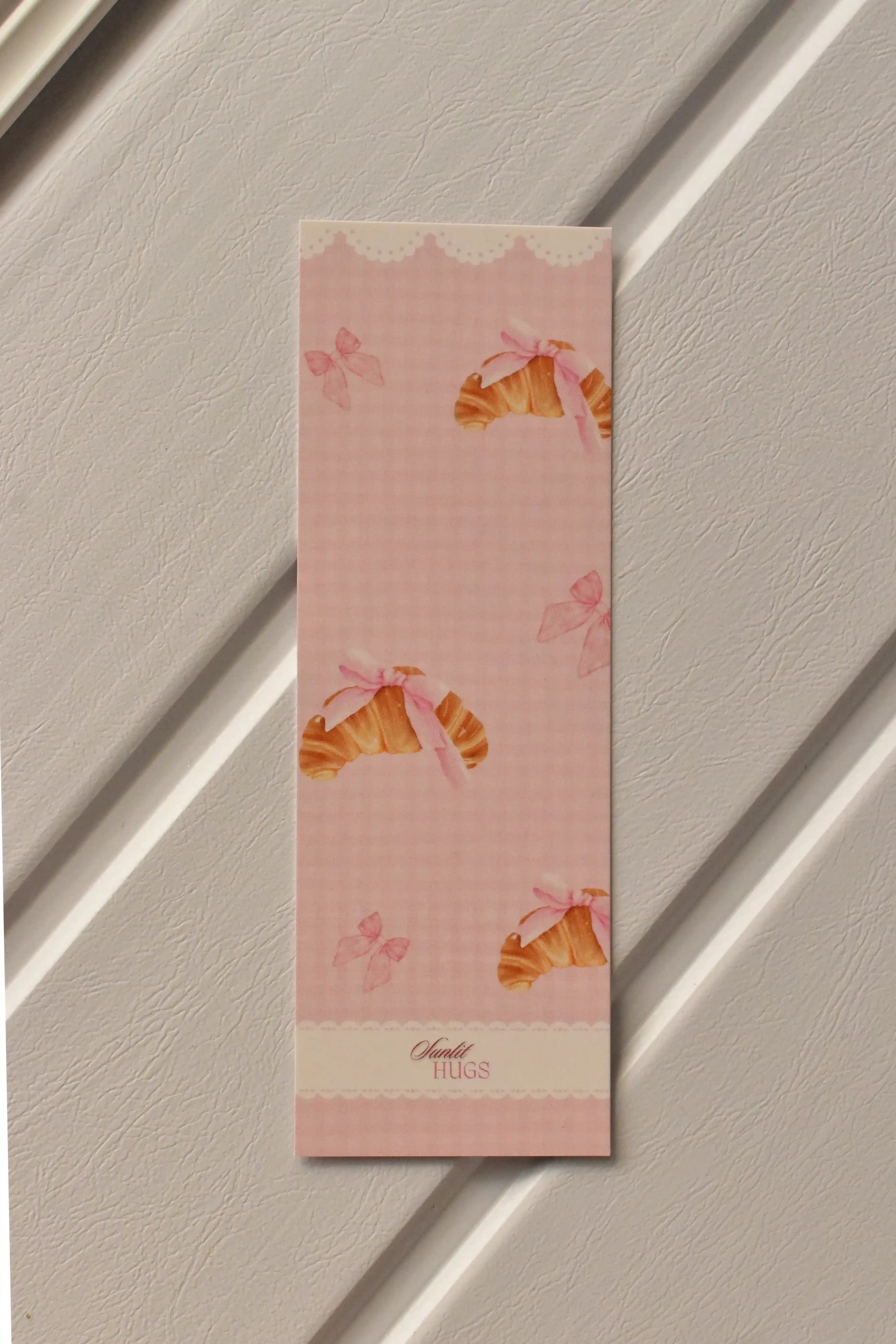 This image shows a detailed, centered view of the Croissant Bookmark front, highlighting the soft pastel pink colour and the charming croissant illustration.