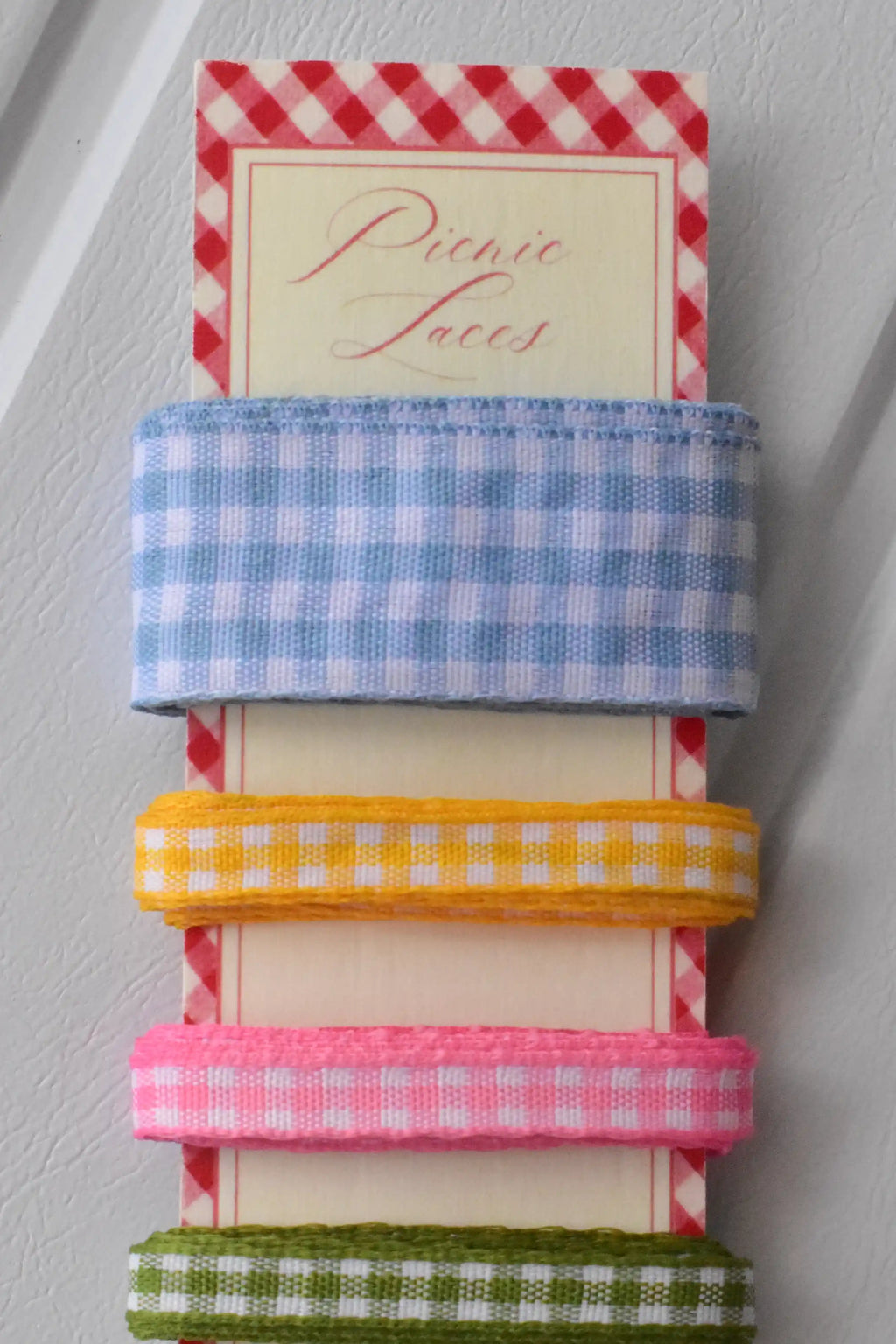 Close-up stack of the top three narrow gingham ribbons in blue, yellow, and pink, showing the texture of the weave.