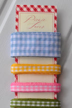 Close-up stack of the top three narrow gingham ribbons in blue, yellow, and pink, showing the texture of the weave.
