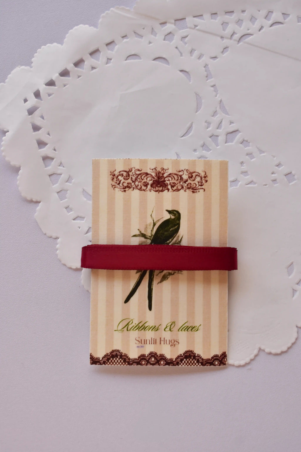 Narrow cherry red satin ribbon (6mm, 2 Metres) draped elegantly around a "Sunlit Hugs" card with a long, loose strand flowing below.