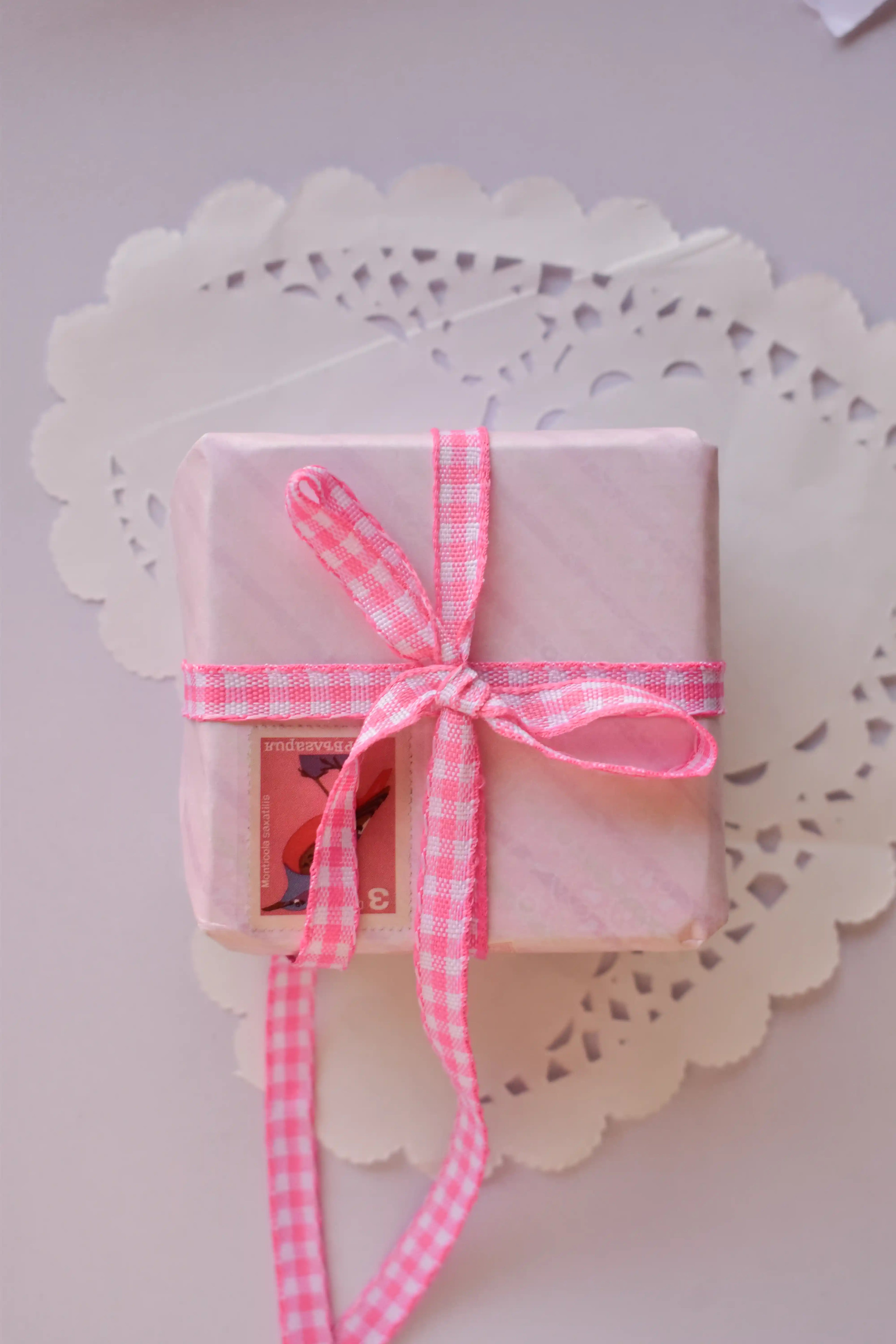 A small, pink striped gift box tied with a narrow pink and white gingham ribbon (2 Metres) bow.