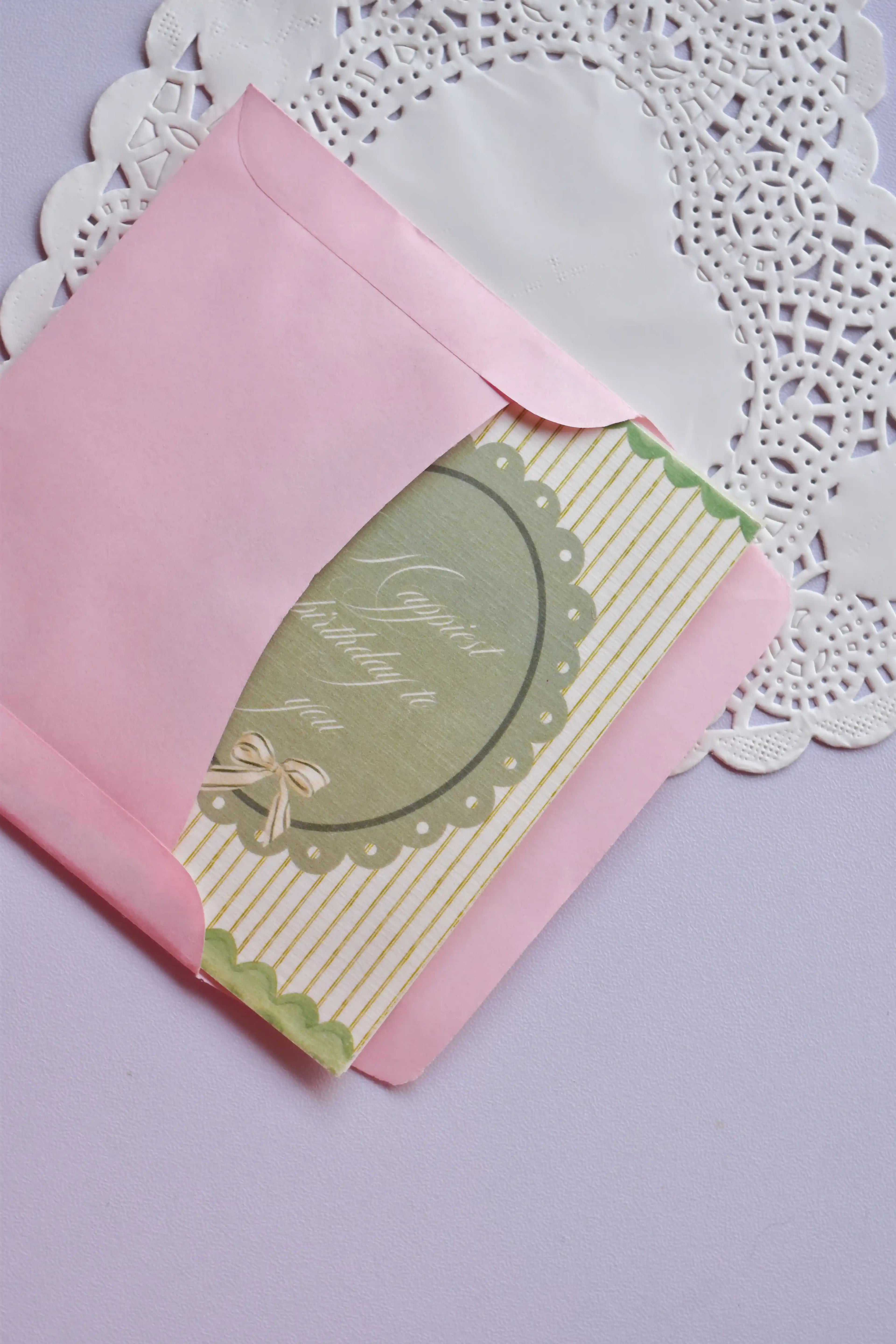 A green and white striped vintage-style birthday card, with a central oval reading "Happiest birthday to you," being placed into an open pink envelope.