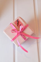 This image shows a beautifully wrapped gift box, featuring the Petal Satin ribbon tied into a delicate bow. The ribbon's elegant pink colour adds a cheerful and charming touch to the present.