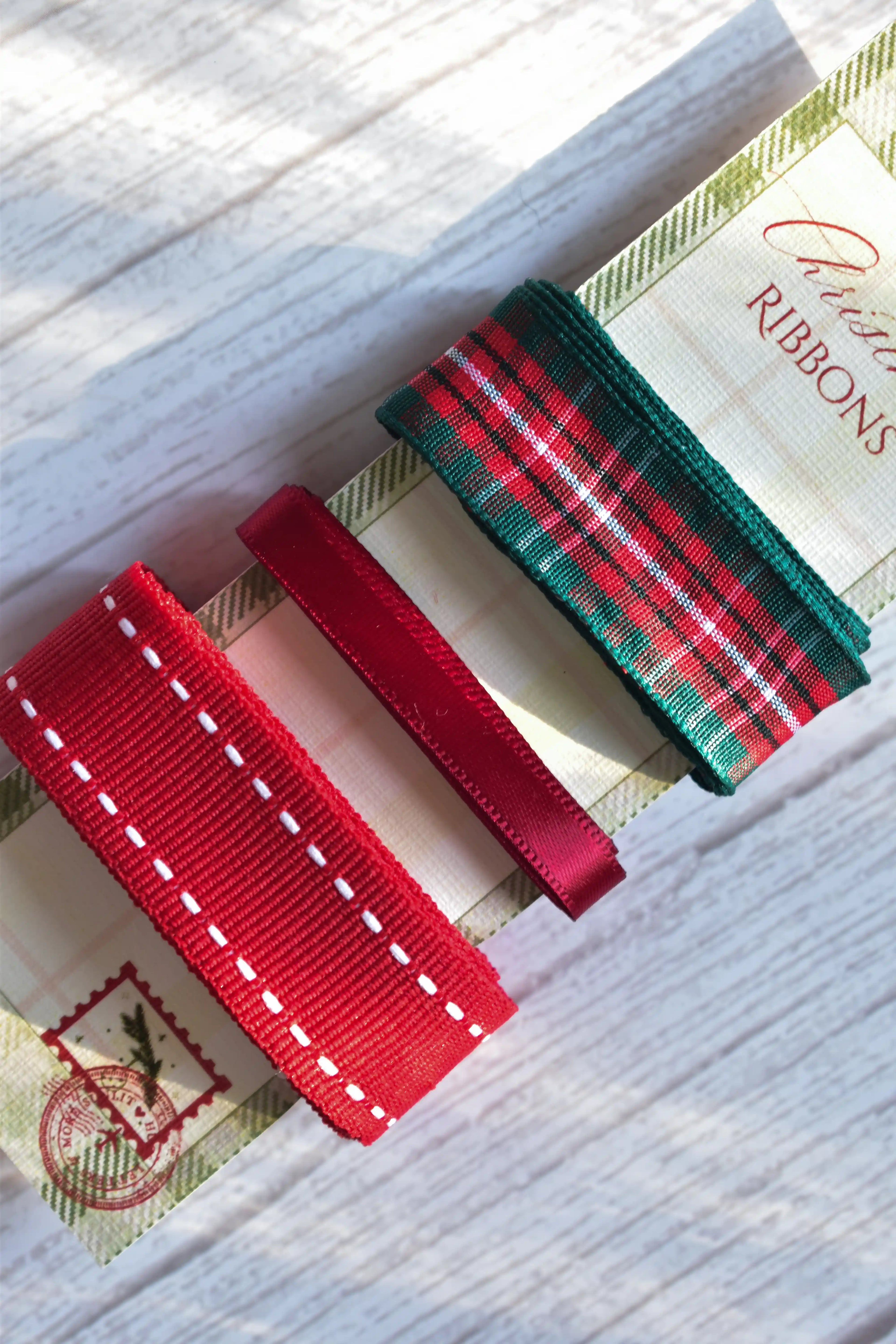 Extreme close-up of the three Christmas ribbons (green plaid, red satin, and red stitched) on their festive card stock label.