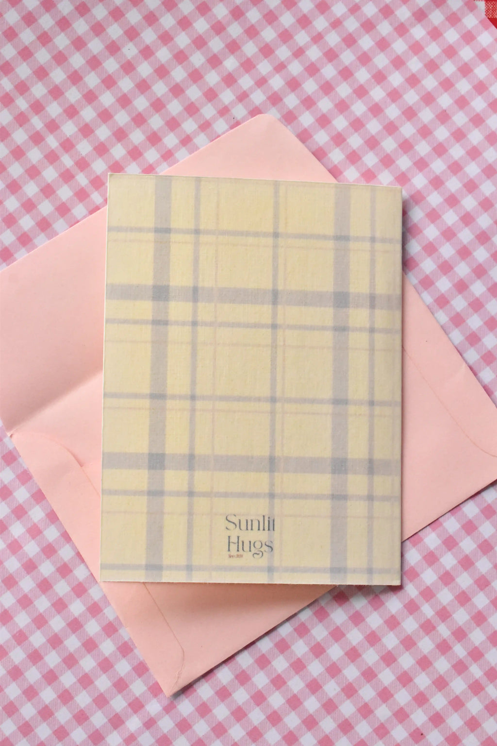 This image displays the back of the 'Glowing Girl Era' card, showing the continuous light purple and white plaid pattern and the Sunlit Hugs brand logo.