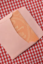 This view captures the Happy Anniversary card being neatly placed into the pink envelope. It demonstrates the presentation, with the elegant peach lace design peeking out as it is prepared for sending a heartfelt message.