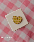 One heart-shaped wooden button with a green and yellow plaid pattern, resting on a white block.