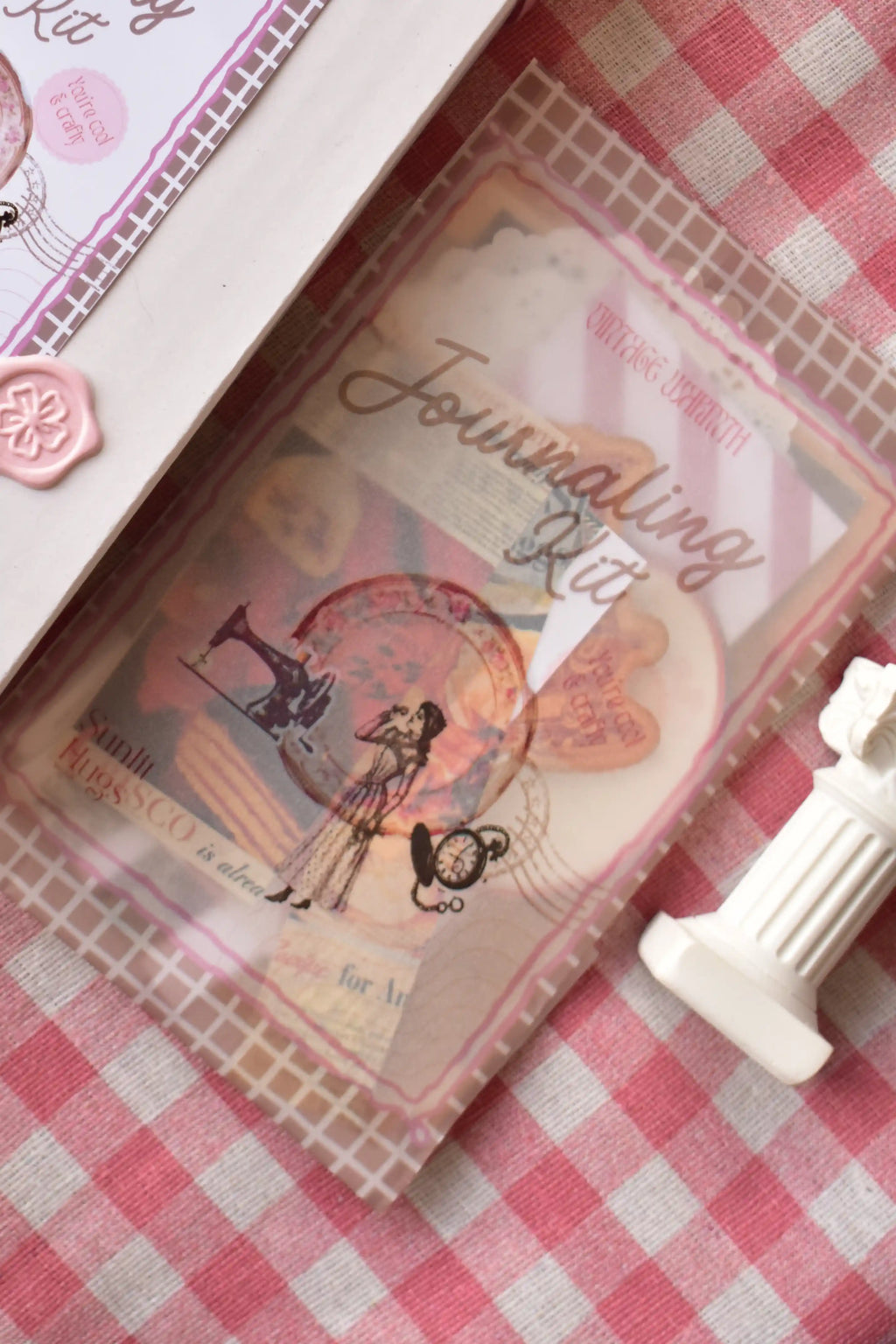 Close-up of the Journaling Kit contents sealed in a clear plastic sleeve, showing vintage figures and papers inside.