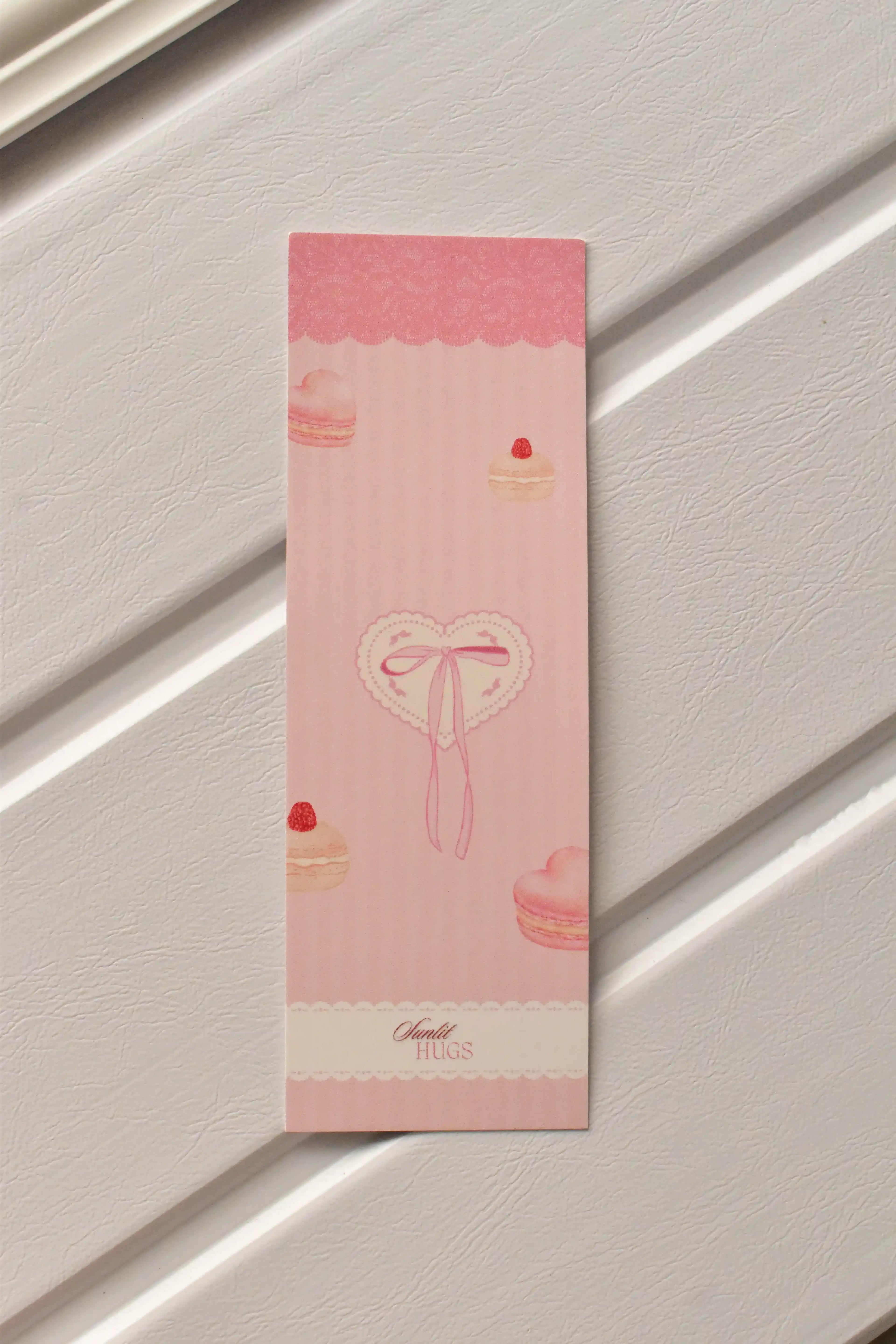 A detailed view of one of the three bookmarks, highlighting the sweet macaron and heart motif and the delightful pastel pink colour.