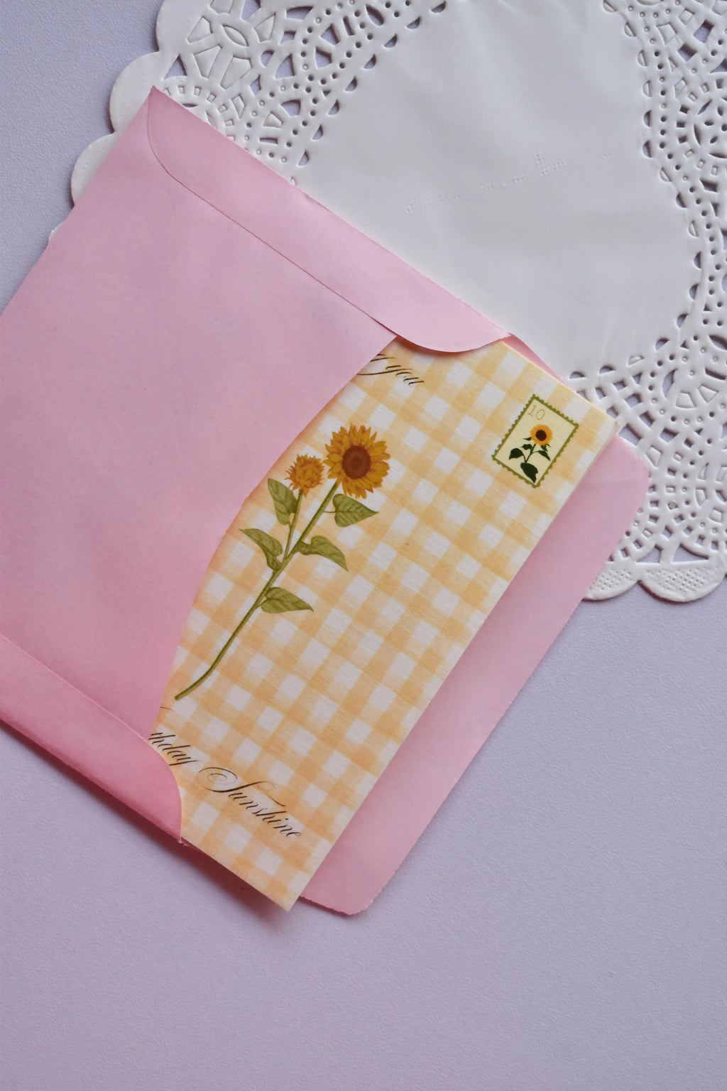 The Mini Birthday Sunshine Card with sunflower and yellow gingham design being gently tucked into the pink envelope.