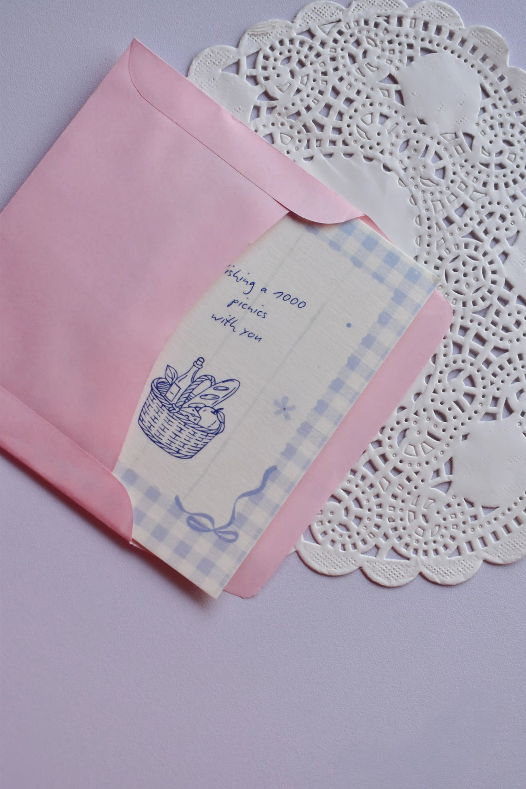 The Mini Wishing Picnics Card being gently tucked into the pink envelope, showing the blue gingham and basket illustration.