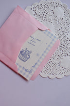 The Mini Wishing Picnics Card being gently tucked into the pink envelope, showing the blue gingham and basket illustration.