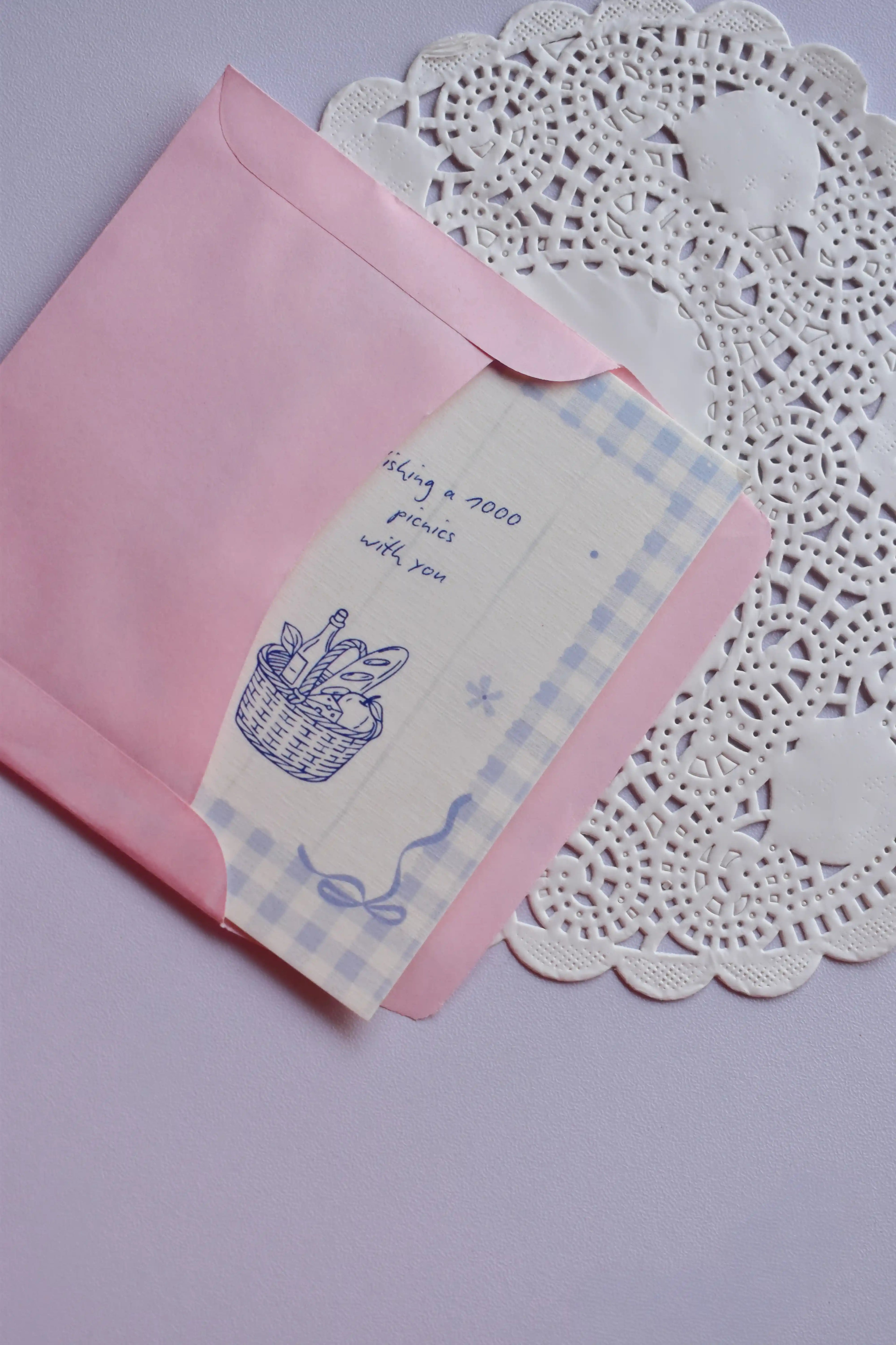 The Mini Wishing Picnics Card being gently tucked into the pink envelope, showing the blue gingham and basket illustration.