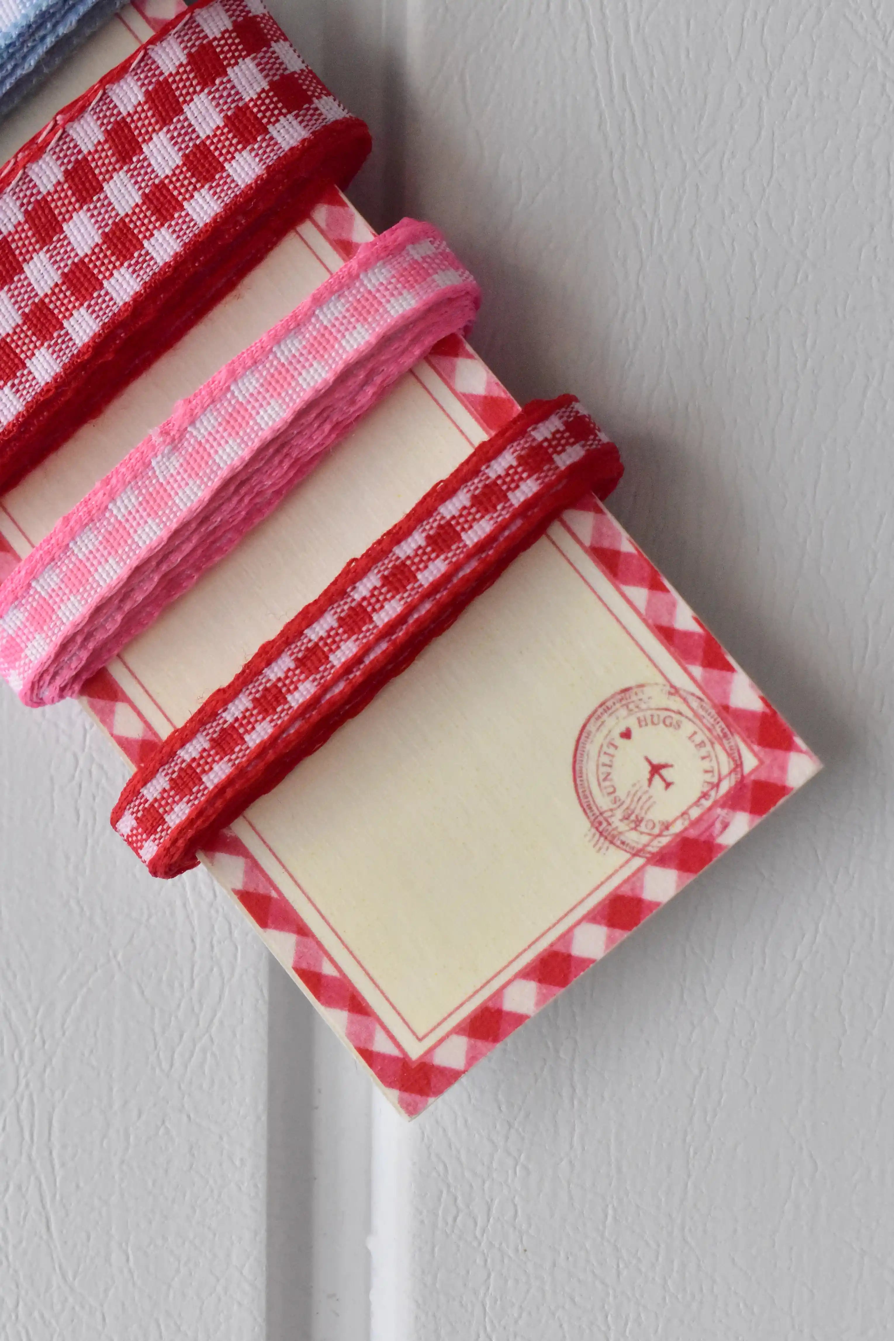 Angled close-up showing the three narrow ribbons (red, pink, red) and the themed display card with a stamp motif.