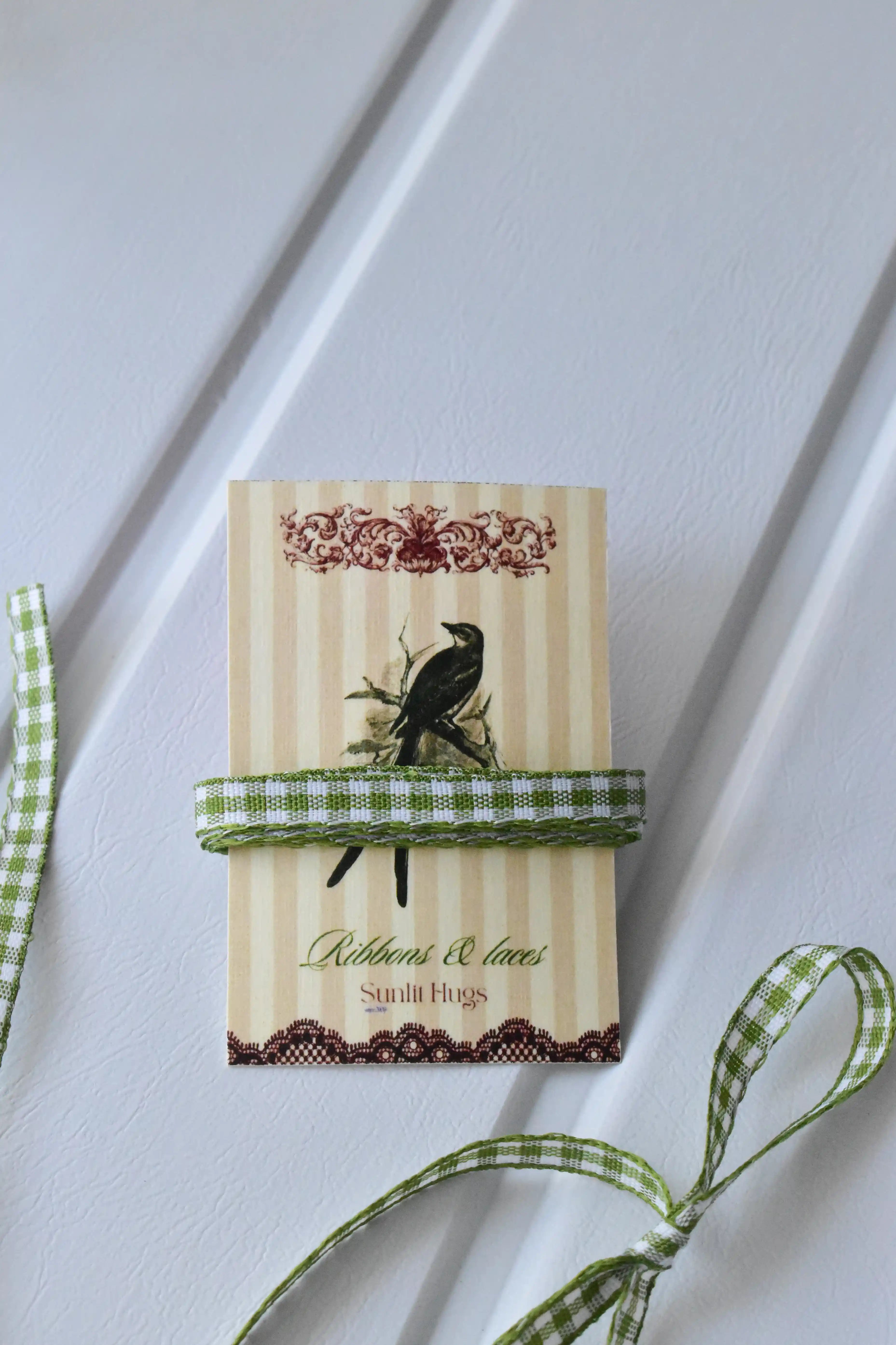 This image displays the Pine Picnic ribbon, showcasing its beautiful green and white checkered design and woven texture. A long strand is loosely unravelled to highlight the full design, with a section wrapped around a "Sunlit Hugs" brand tag.