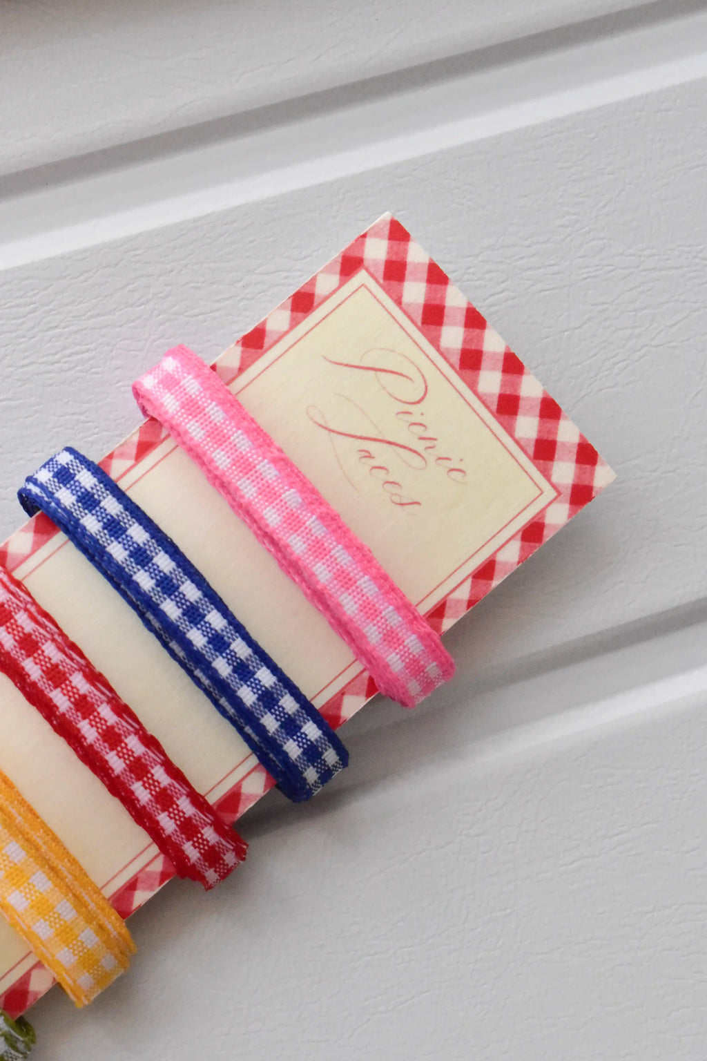Angled close-up showing the pink, blue, and red narrow gingham ribbons, emphasizing the "Picnic Laces" text on the display card.
