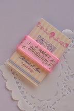 Angled view of the soft pink birthday ribbon wrapped around a "Sunlit Hugs" card, emphasizing the ribbon's texture and gold foil script.