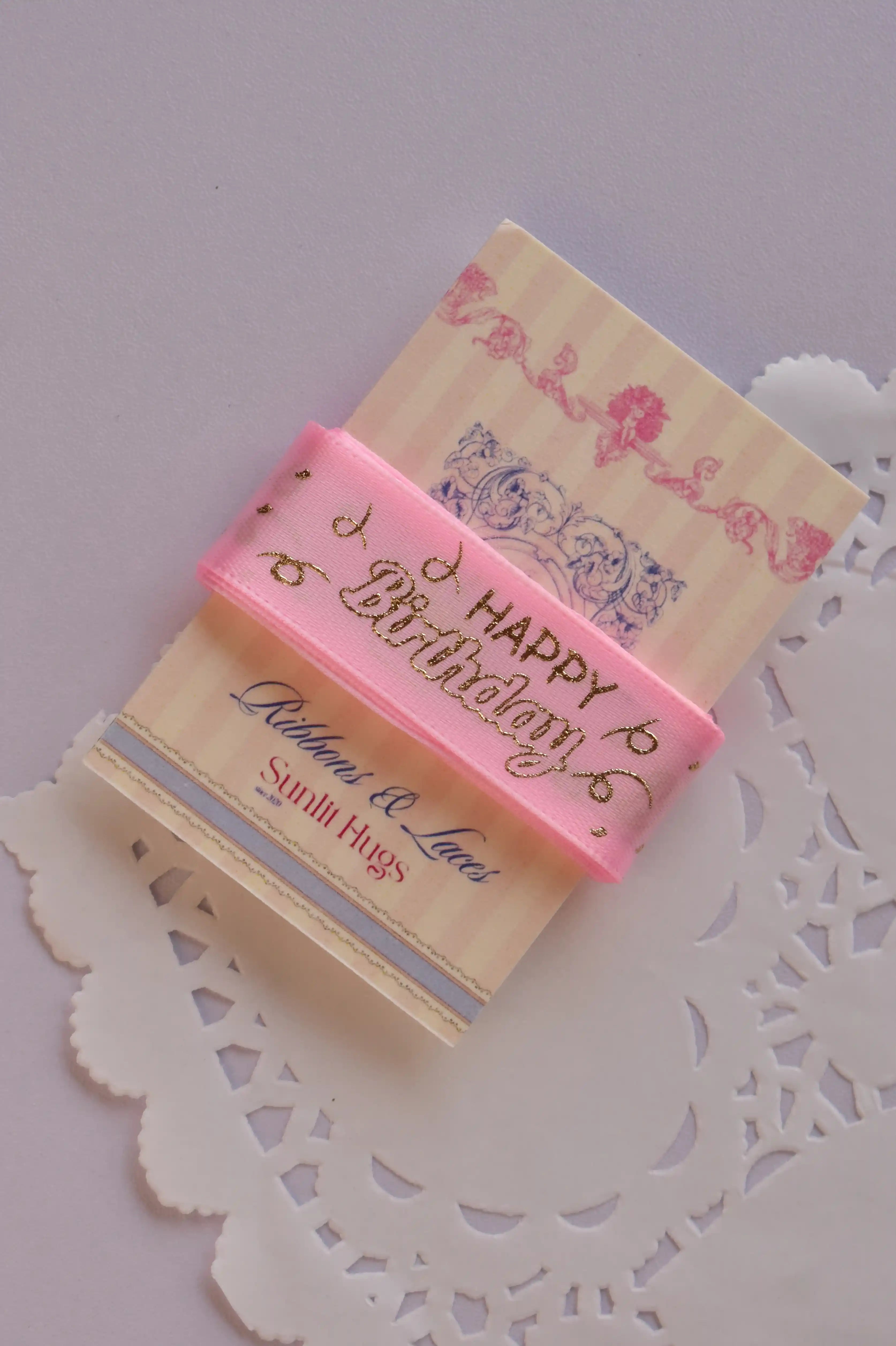 Angled view of the soft pink birthday ribbon wrapped around a "Sunlit Hugs" card, emphasizing the ribbon's texture and gold foil script.