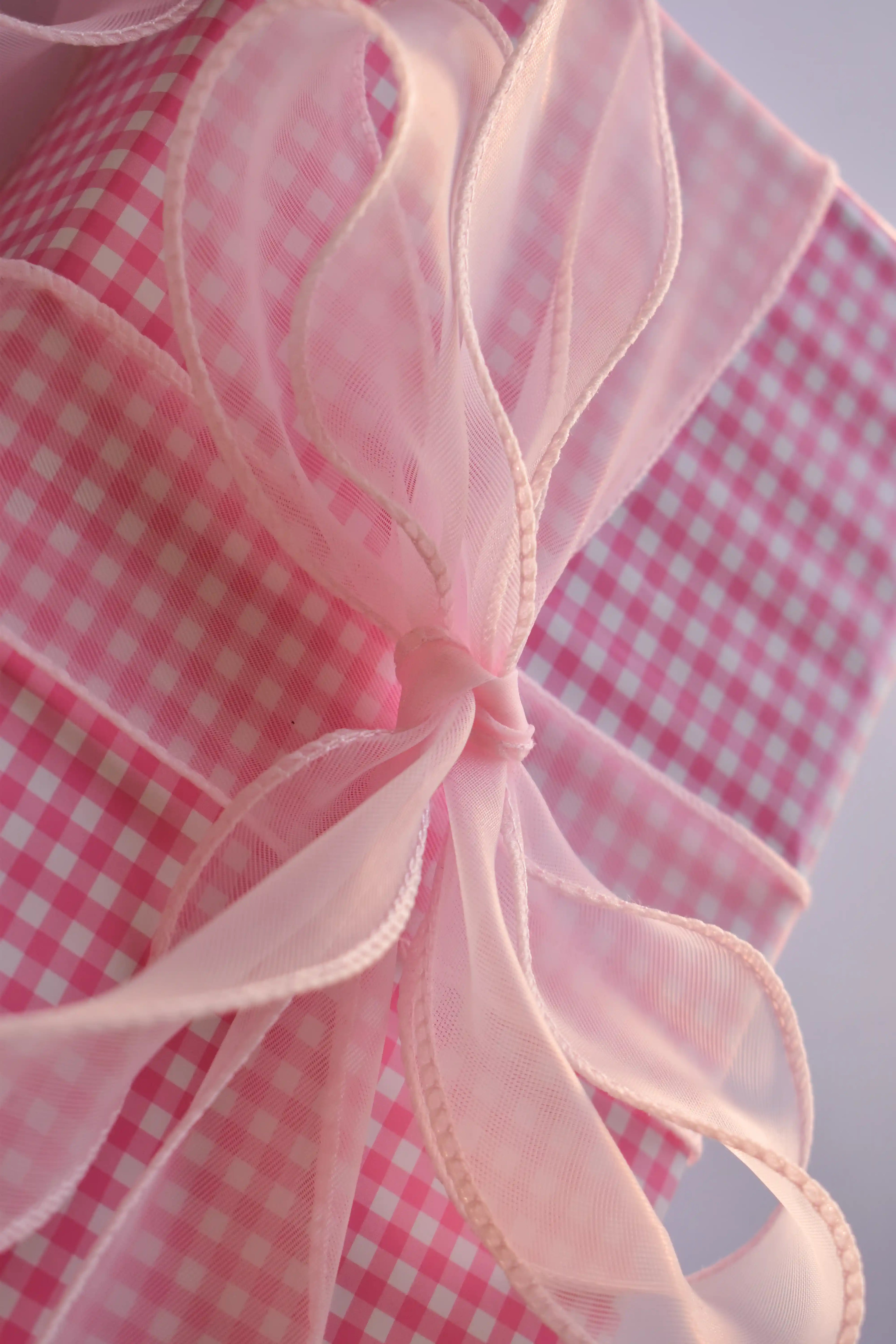 Extreme close-up of a large, high-volume bow made from the wide pink sheer organza ribbon, tied around pink gingham wrapping paper.