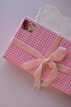 A pink checkered gift box wrapped with a soft pink velvet ribbon tied in a large, luxurious bow.