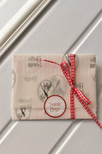 This image showcases the thoughtful gift-wrapping for the postcard, using Sunlit Hugs branded vellum paper and a sweet gingham ribbon to ensure a high-quality presentation.