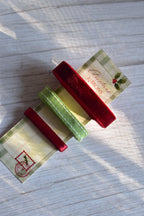 A set of three premium Christmas ribbons, deep red velvet, green stitched grosgrain, and thin red satin, displayed on a postal-themed card stock label.