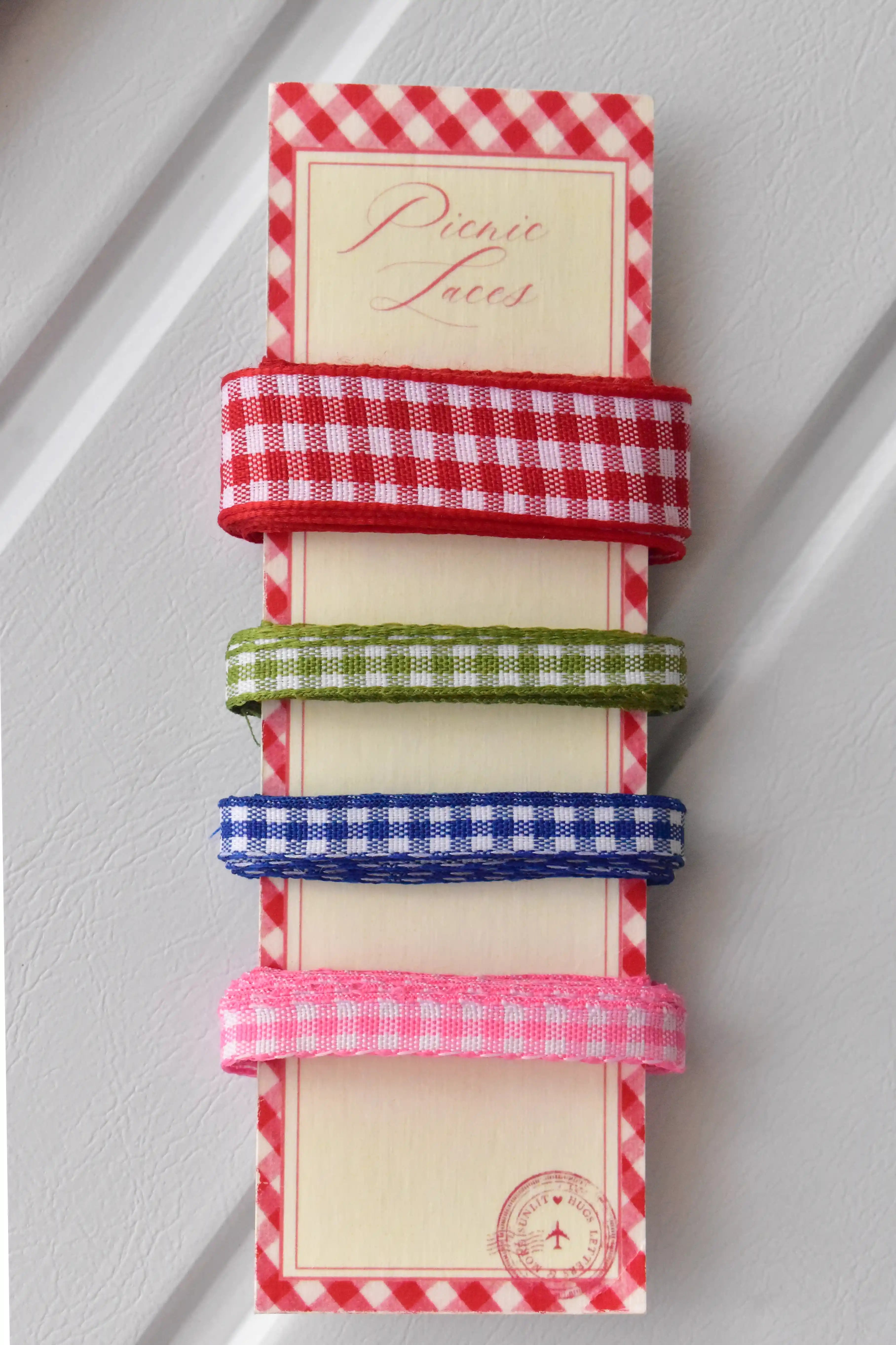 Four narrow gingham ribbons in red, green, blue, and pink, displayed vertically on a themed ribbon card.