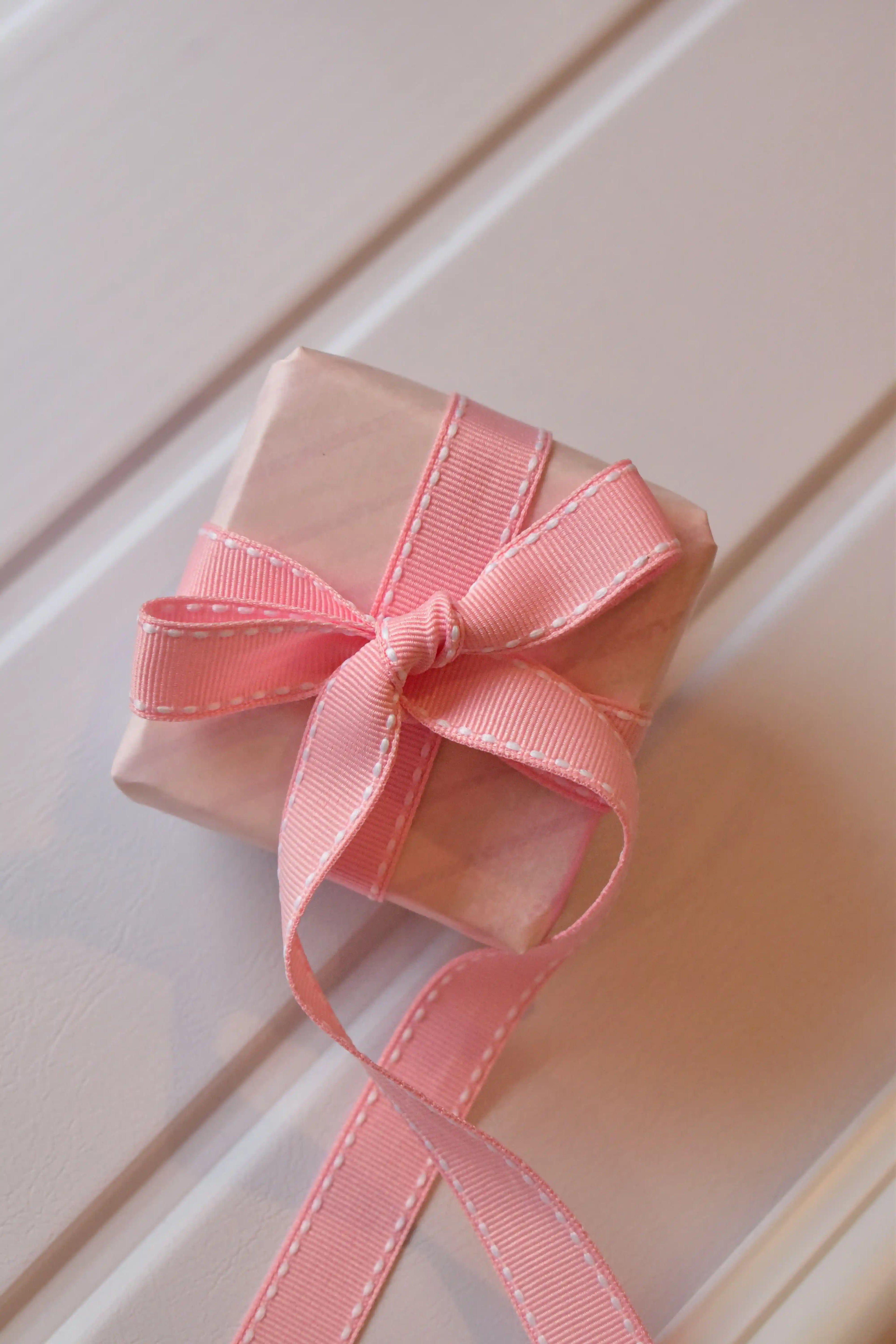 This image shows a beautifully wrapped gift box, featuring the Rose Taffy ribbon tied into a lovely bow. The ribbon's sweet pink colour and subtle stitching add a charming touch to the present.