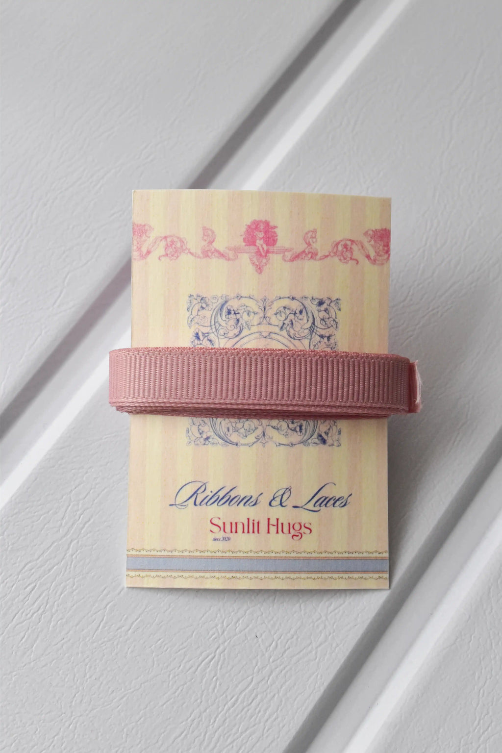This detailed, head-on view of the Rustic Blush ribbon highlights its sophisticated rose gold colour and subtle texture. The ribbon is wrapped tidily around the "Sunlit Hugs" brand tag to show its precise design.
