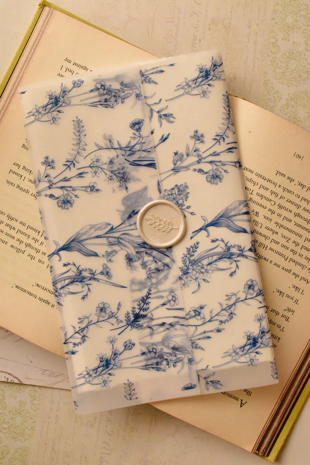 A detailed, top-down view of the Midnight Dream Letter, capturing the quiet beauty of the blue and white floral vellum and the delicate ivory wax seal on the surface of the open book.