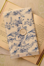 A detailed, top-down view of the Midnight Dream Letter, capturing the quiet beauty of the blue and white floral vellum and the delicate ivory wax seal on the surface of the open book.